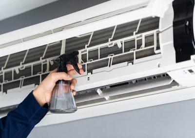 Uma pessoa com um borrifador a limpar o interior de um aparelho de ar condicionado